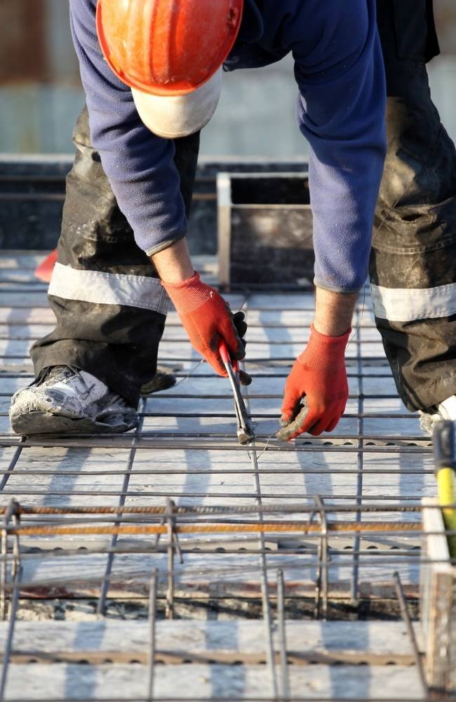 Construction worker ties rebar on site.