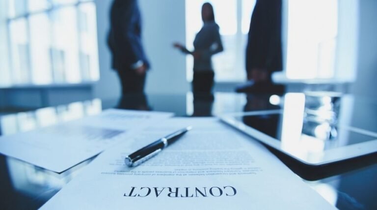 Contract document on table with blurred figures discussing.