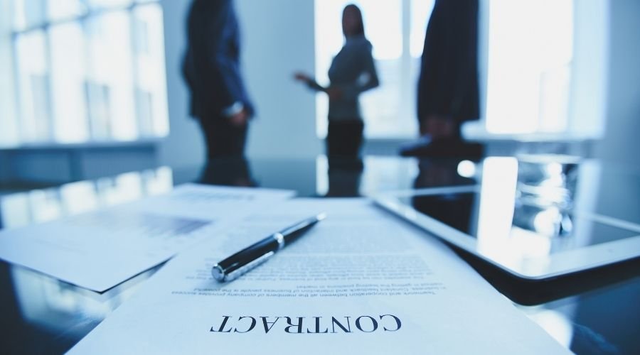 Contract document on table with blurred figures discussing.